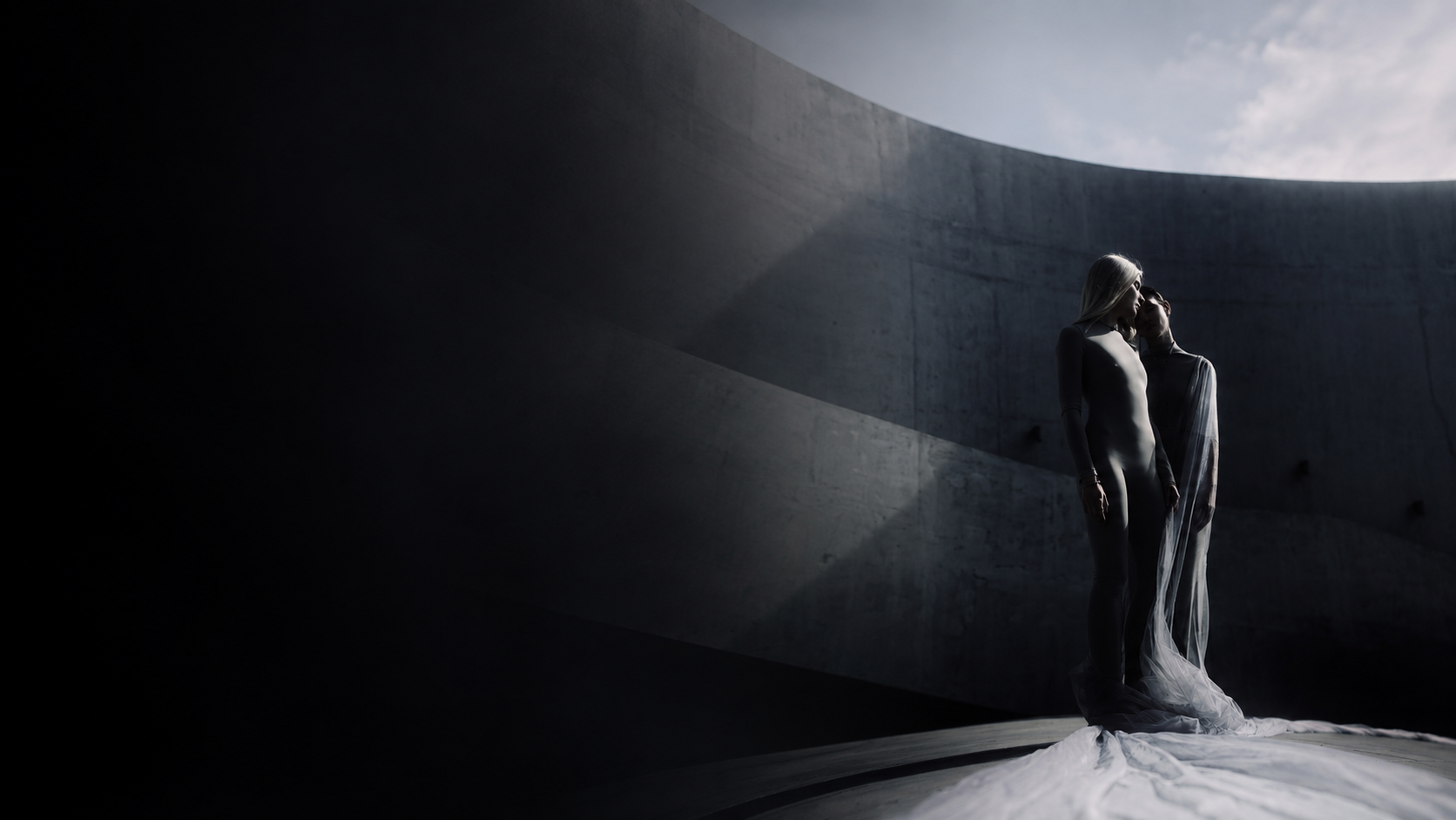 Cinematic editorial photograph — two figures against a curved concrete wall